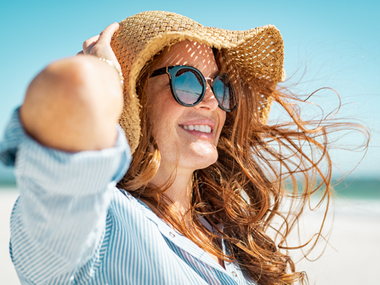 Female smiling while wearing sunglasses and a hat at the beach