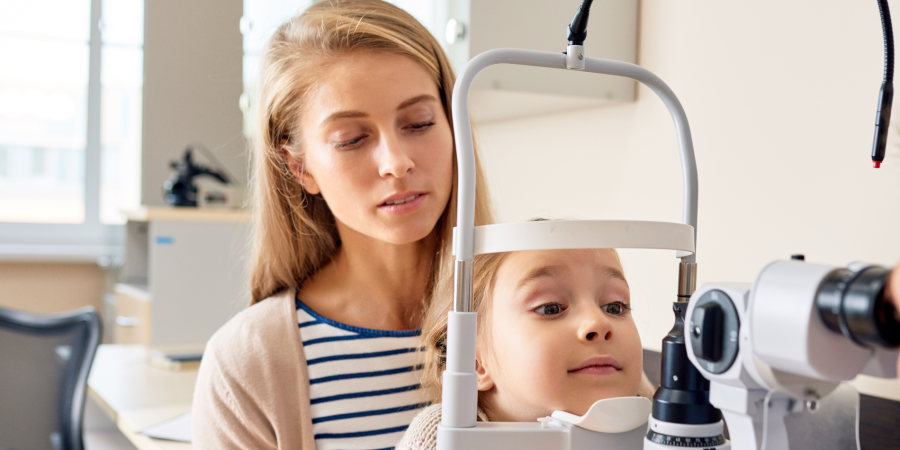 Mom assisting daughter as daughter receives an eye exam